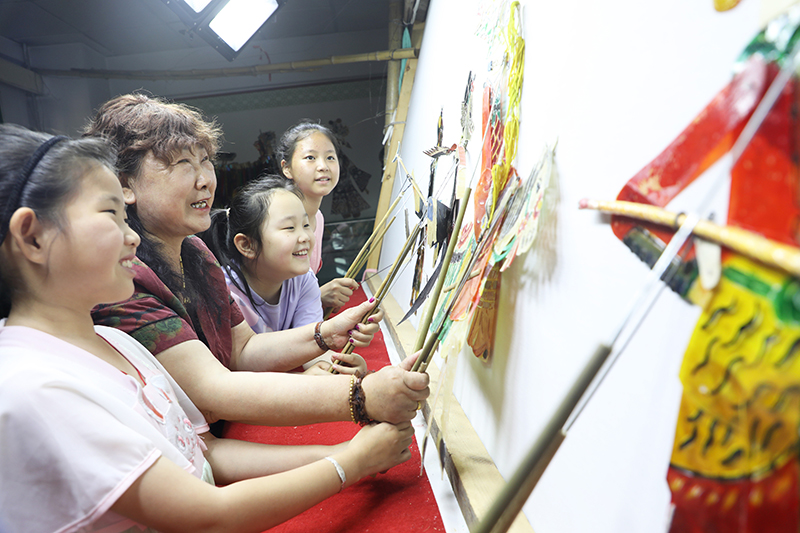 皮影藝人指導小朋友表演皮影戲。